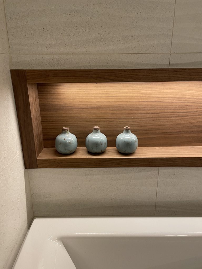 Close-up of a wooden bathroom niche with decorative ceramic vases above a bathtub, exemplifying attention to detail in interior design by Campo Design in Victoria, BC.