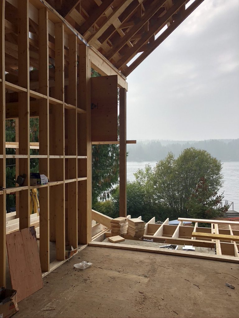 Framing stage of a custom home construction with a scenic water view, showcasing the build and design expertise of Campo Design in Victoria, BC.