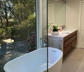 Elegant bathroom featuring a freestanding bathtub with a garden view, modern vanity, and large mirror, showcasing luxurious bathroom design and renovation services in Victoria, BC by Campo Design.