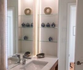 Modern bathroom vanity with glass shelves displaying decorative ceramics and a large mirror, highlighting elegant bathroom design in Victoria, BC by Campo Design.