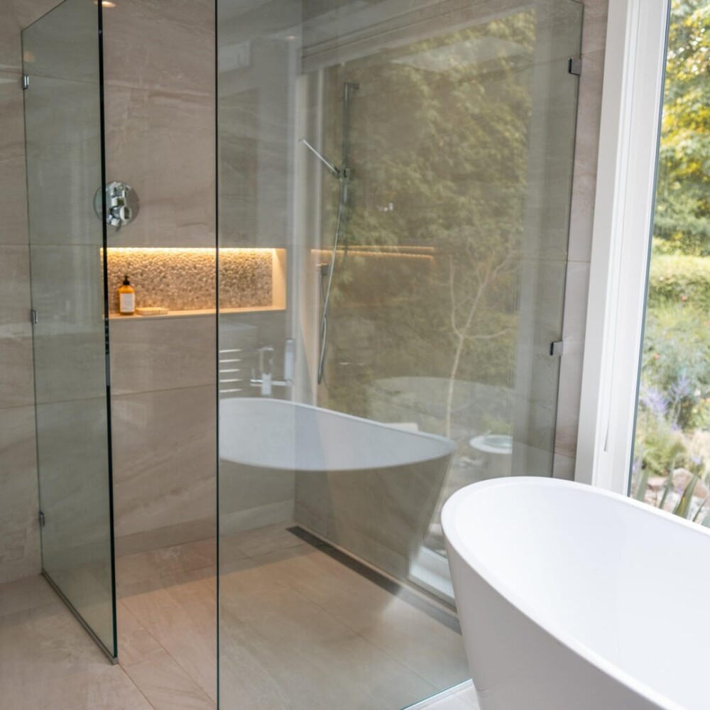 Modern bathroom with glass-enclosed shower, freestanding bathtub, and large window overlooking a garden, showcasing luxury bathroom renovation and design services in Victoria, BC by Campo Design.