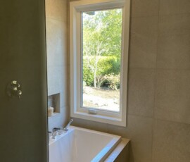 Spacious bathroom featuring a freestanding bathtub beside a large window, modern vanity with double sinks, and glass-enclosed shower, exemplifying premium bathroom design and renovation by Campo Design in Victoria, BC.